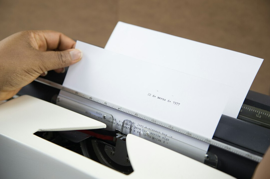 Close-up of hands typing on a laptop keyboard next to printed documents